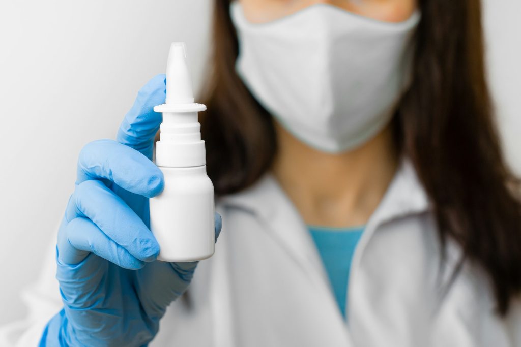 A woman using nose spray for flu treat or running nose holds medicine in the hand. Doctor in