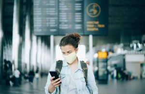 Young woman traveler wearing a face mask jn the airport and using mobile phone